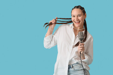 Young woman with dreadlocks and microphone singing on blue background