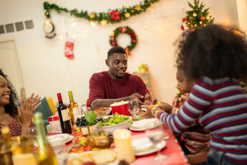 A warm Christmas family dinner with a father serving food to his young child, surrounded by festive decorations, a Christmas tree, and a holiday table spread. Joyful and cozy holiday atmosphere.