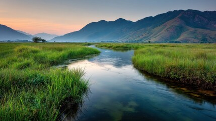Fototapeta premium Serene river winding through a grassy meadow with distant mountains.
