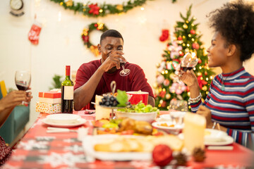 A family enjoys a festive Christmas dinner, sharing food and creating memories. A beautifully decorated Christmas tree and wreath add warmth, while candles and decor enhance the cozy holiday setting.