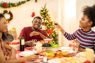 A family enjoys a festive Christmas dinner, sharing food and creating memories. A beautifully decorated Christmas tree and wreath add warmth, while candles and decor enhance the cozy holiday setting.