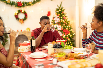 A family enjoys a festive Christmas dinner, sharing food and creating memories. A beautifully decorated Christmas tree and wreath add warmth, while candles and decor enhance the cozy holiday setting.