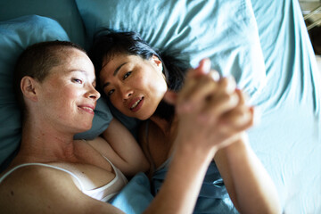 Young lesbian couple lying down in their bed in the bedroom in the morning