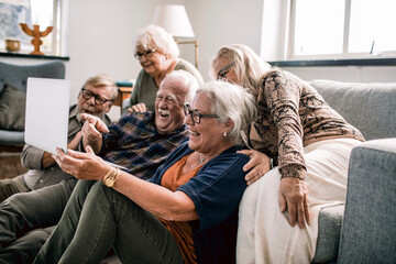 Group of senior friends laughing together while watching something on laptop