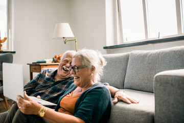 Senior couple laughing together while watching something on laptop at home
