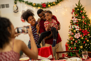 An African American family gathers for a festive Christmas party, enjoying snacks, drinks, and laughter in their decorated living room. Concept for holiday entertaining and joyful feasts.