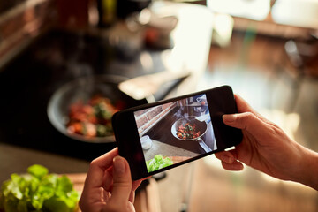Young woman using a smart phone to take a photo of a meal she is cooking and preparing in the kitchen