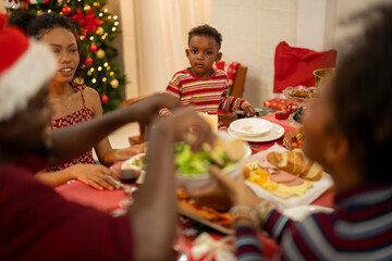An African American family gathers for a festive Christmas party, enjoying snacks, drinks, and laughter in their decorated living room. Concept for holiday entertaining and joyful feasts.