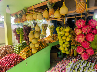 Traditional fruit stall in Indonesia with various tropical fruits arranged and hanging for sale.