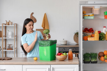 Beautiful woman throwing spoiled food from fridge in kitchen