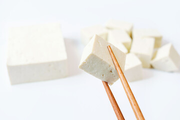 Piece of tofu in wooden chopsticks on white background close-up.