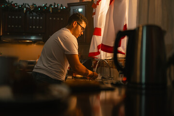 Latino young man washing dishes in cozy Christmas kitchen