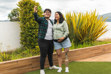 Happy pregnant woman with prosthetic leg taking selfie with husband in garden