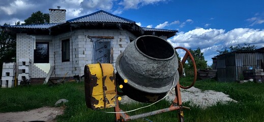 Construction project featuring concrete mixer at a house site on a sunny afternoon with cloudy skies