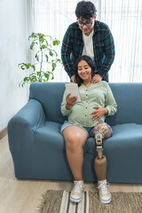 Pregnant woman with prosthetic leg using tablet and receiving support from husband, they happily watch content on a tablet