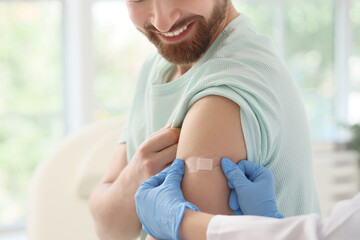 Young man receiving medical patch from doctor after vaccination in clinic, closeup