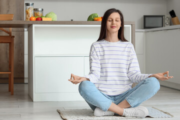 Young woman meditating on rug in kitchen