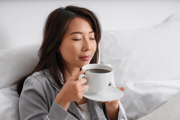 Young Asian woman with cup of coffee in bedroom, closeup