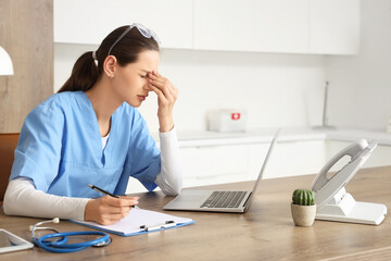 Tired female medical intern studying at table in clinic