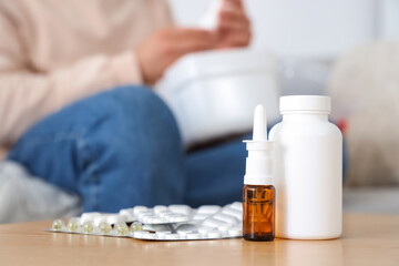 Pills and nasal drops on table against man with first aid kit at home, closeup