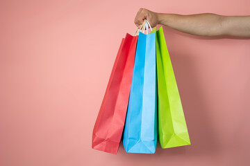 Male hand holding three shopping bags on a pink background, shopping concept with copyspace