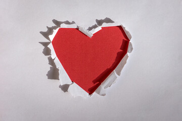 Heart shape red hole torn through paper. Copy space.