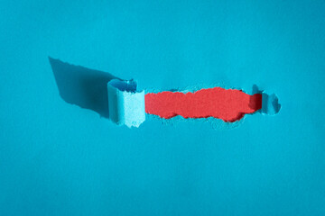 Hole ripped in blue paper on red background. Copy space.