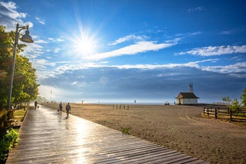 wooden boardwalk beside sand beach in morning with bright sunlight after rain with people in...