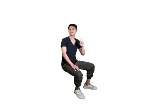 A young man in casual attire is captured mid-air in a squatting pose, looking down at his hands against a white background.