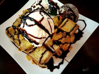 Honey toast with vanilla and chocolate ice cream drizzled with chocolate syrup on white plate – popular Thai fusion dessert