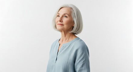 An elderly woman in a casual tunic posing with a thoughtful gaze upward on a white background