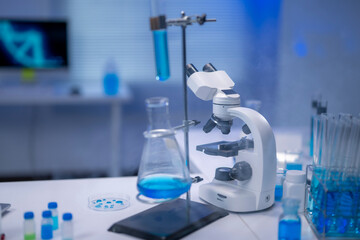 Modern microscope and laboratory glassware with blue chemical liquid for scientific experiment