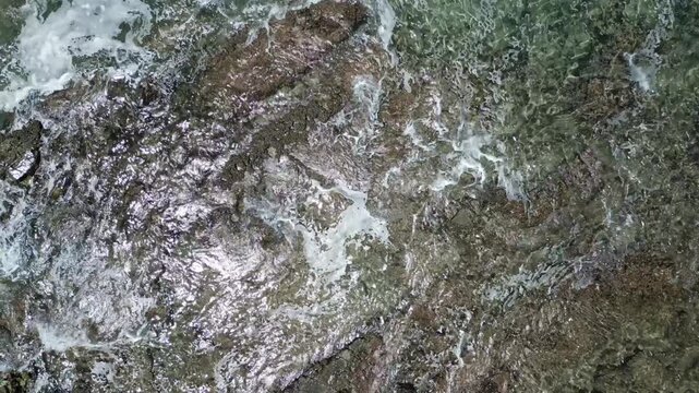 Looking down on the green water lapping calmly into the rocks and moving out into deeper water with heavier waves crashing into the rocks.