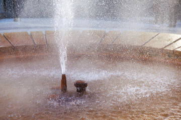 Circular water fountain with stone rim and splashing jets in sunlight, geyser