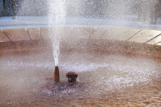 Circular water fountain with stone rim and splashing jets in sunlight, geyser - Powered by Adobe