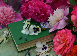 Still life with green book and flowers of peony and pansy on the table in the garden. Romantic, vintage home and greeting card concept