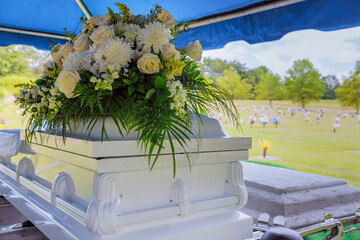 Floral arrangement atop an elegant casket at peaceful burial site surrounded by gravestones