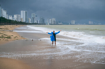 man in a raincoat on beach by the sea with waves in cloudy weather with rain. Concept of the rainy...