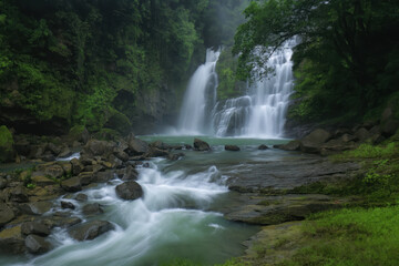 Waterfall with flowing river and rocks surrounded by lush green forest creating peaceful scene