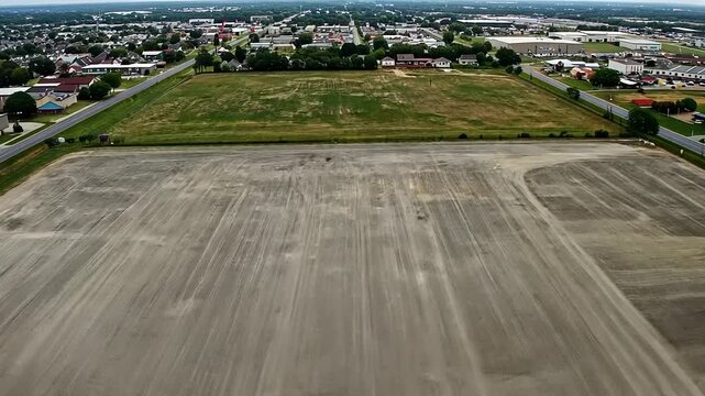 Aerial view of a large, empty lot with tire tracks and scattered debris near a suburban area