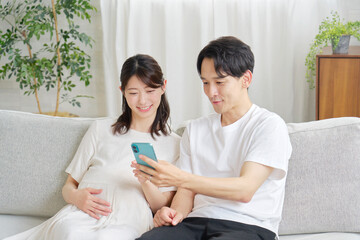 リビングでスマホを使う妊娠中の妻と夫