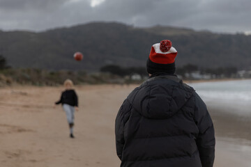 Father and son kicking an Australian rules football on a beach in winter with coats and beanie