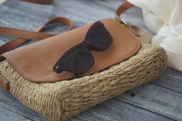 Stylish woven bag with sunglasses on wooden table