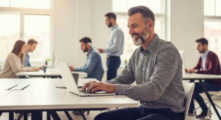 Focused businessman working on a laptop in a bright open-plan office environment surrounded by colleagues