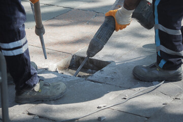 Workers repair pavement using a jackhammer in a city street