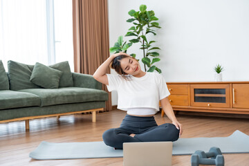 Young Asian woman stretching yoga workout on exercise mat while online training class with computer...