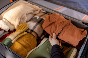 A woman's hand packing winter clothes and accessories in suitcase