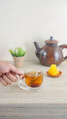 Hand holding a clear glass cup of tea with teabag on wooden table isolated on white background