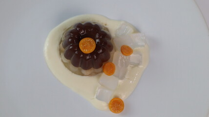 chocolate coconut pudding on a white plate with small orange fruit topping