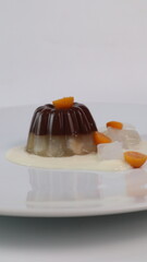 chocolate coconut pudding on a white plate with small orange fruit topping